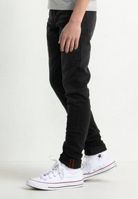 Černé slim-fit džíny vyrobené z denimu, s hladkou texturou. Kombinované s bílými vysokými teniskami se červenými akcenty a černými tkaničkami.