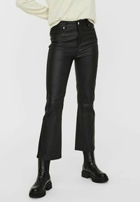 Svarta fusk läderflarebyxor med hög midja, med framfickor och en slät yta, tillsammans med svarta ankle boots.