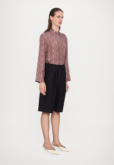 Pitkähihainen vaaleanpunainen paita, jossa on geometrinen printti, yhdistetty tummansinisiin denimpö shortsit, joissa on joustava vyötärö ja korostetut saumat. Valkoiset korkokengät.