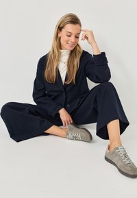 Traje de raya diplomática en color marino con pantalones de pierna ancha y una chaqueta ajustada, combinado con zapatillas en gris claro con cordones y detalles en blanco.