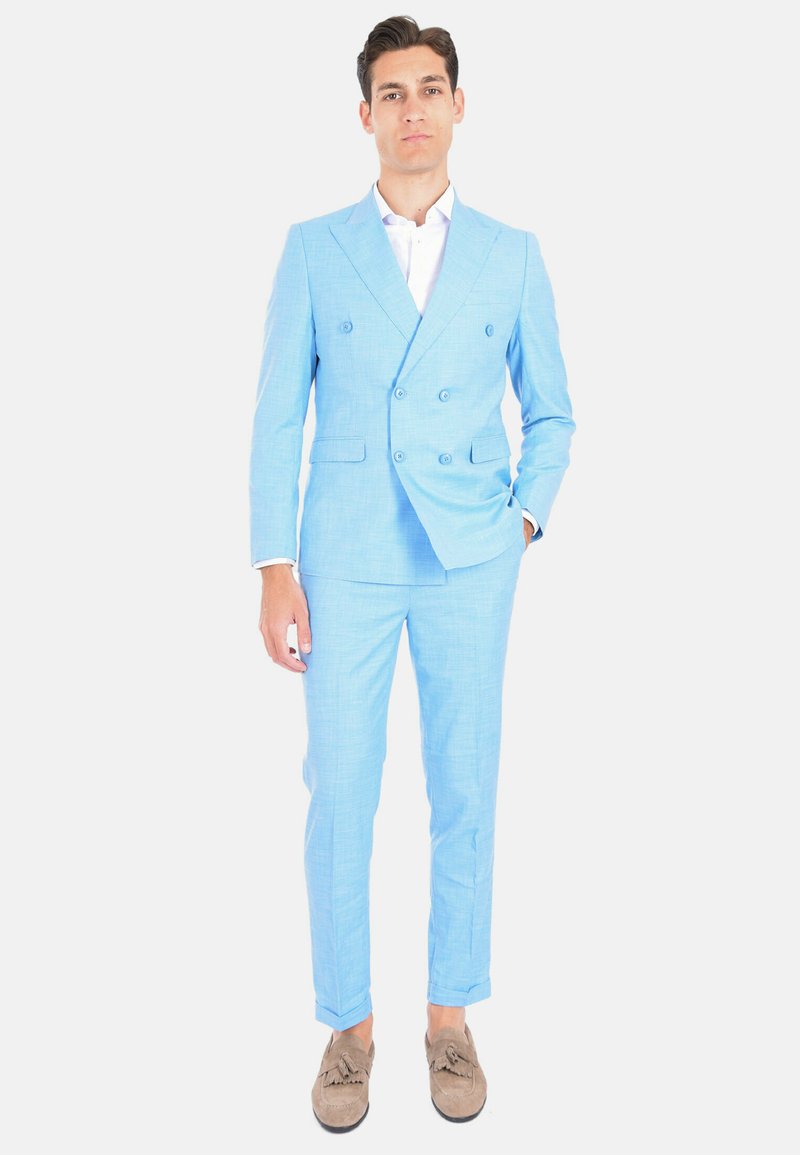 Completo doppiopetto azzurro chiaro in tessuto strutturato, vestibilità slim, pantaloni abbinati e mocassini marroni. Camicia bianca sotto.