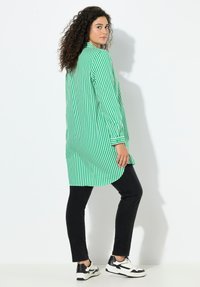 Camisa de rayas verdes y blancas con mangas largas, dobladillo asimétrico, combinada con pantalones ajustados negros y zapatillas negras y blancas.