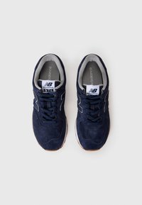 Une paire de baskets New Balance 574 bleu marine avec des étiquettes de logo blanches, les lacets attachés, et une doublure intérieure grise sur un fond blanc.