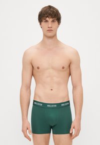 Boxer briefs em mistura de algodão verde com um cós branco com o logótipo "HOLLISTER", apresentando um design ajustado e uma textura suave. Sem padrões ou acessórios.