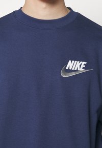 Sudadera azul marino de algodón suave con cuello de canalé. Presenta un logotipo de Nike bordado en blanco en el lado izquierdo del pecho.