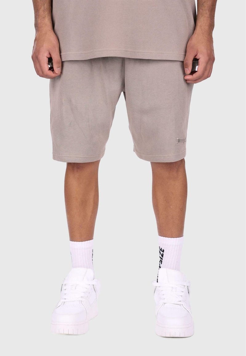 Beige teksturerede shorts med et afslappet fit, parret med hvide sneakers og hvide ribbede sokker med sorte bogstaver.