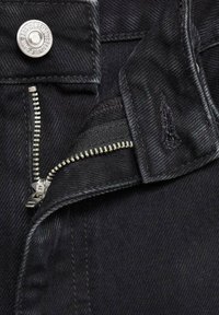 Črn denim material z enim srebrnim gumbom in delno odprtim kovinskim zadrgo. Vidne so čiste šivane podrobnosti na robovih.