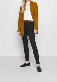 Sinappikeltainen bleiseri valkoisen t-paidan päällä, mustat kapeat farkut ja mustat loaferit. Vyössä on ruskeita yksityiskohtia, ja kokonaisuus on tyylikkään siro.