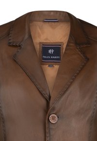 Brun læderblazer med omvendt krave, enkelt knaplukning og synlige syninger. Indersiden har et tan-for med brandlabel.