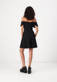 Černé šaty bez ramínek s přiléhavým vrškem a rozšířenou sukní. Hladká tkanina s zipem na zadní straně. Kombinováno s černými platformovými botami.