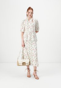 Top peplum a stampa floreale e gonna coordinata in tessuto leggero, con fiori rosa e verdi. Include una borsa crema con dettagli dorati.