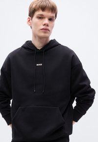 Μαύρο φούτερ με κουκούλα από μαλακό ύφασμα, με μπροστινή τσέπη, ρυθμιζόμενα κορδόνια και μικρό χρυσό λογότυπο "BOSS" στο στήθος.