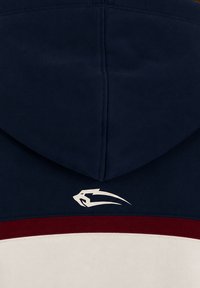 Vêtement à capuche bleu marine avec un logo abstrait de panthère blanche au-dessus d'une bande horizontale bordeaux et blanche.