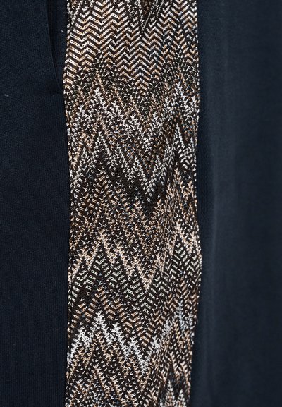 Μαύρο ύφασμα με υφή, με πλευρά με σχέδιο που διαθέτει ριγέ ζιγκ ζαγκ σε μεταλλικό μπρούντζο, ασημί και λευκά νήματα, προσθέτοντας αντίθεση.