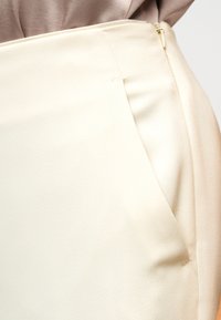 Κρεμ φούστα με λείο ύφασμα, ραμμένη σχεδίαση, πλαϊνή τσέπη και διακριτικό φερμουάρ κλεισίματος, με ελαφρώς δομημένη σιλουέτα.