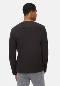 Langærmet sort t-shirt med rund halsudskæring og ribbet tekstur. Har en lige kant og logo-detalje nær siden.