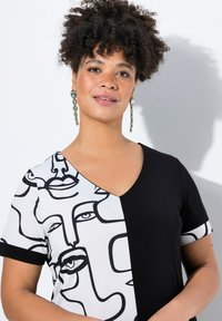 Robe noire et blanche en v avec des designs de visages abstraits sur un côté, tissu lisse, manches courtes avec des bords contrastés.