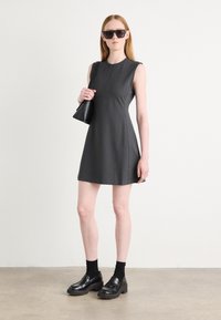 Sleeveless gray dress with a round neckline and front zipper. Paired with black chunky shoes and sunglasses, holding a black handbag.