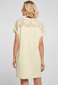 Light yellow short dress with a lace back detail and soft texture. Features cap sleeves and a relaxed fit, reaching mid-thigh.