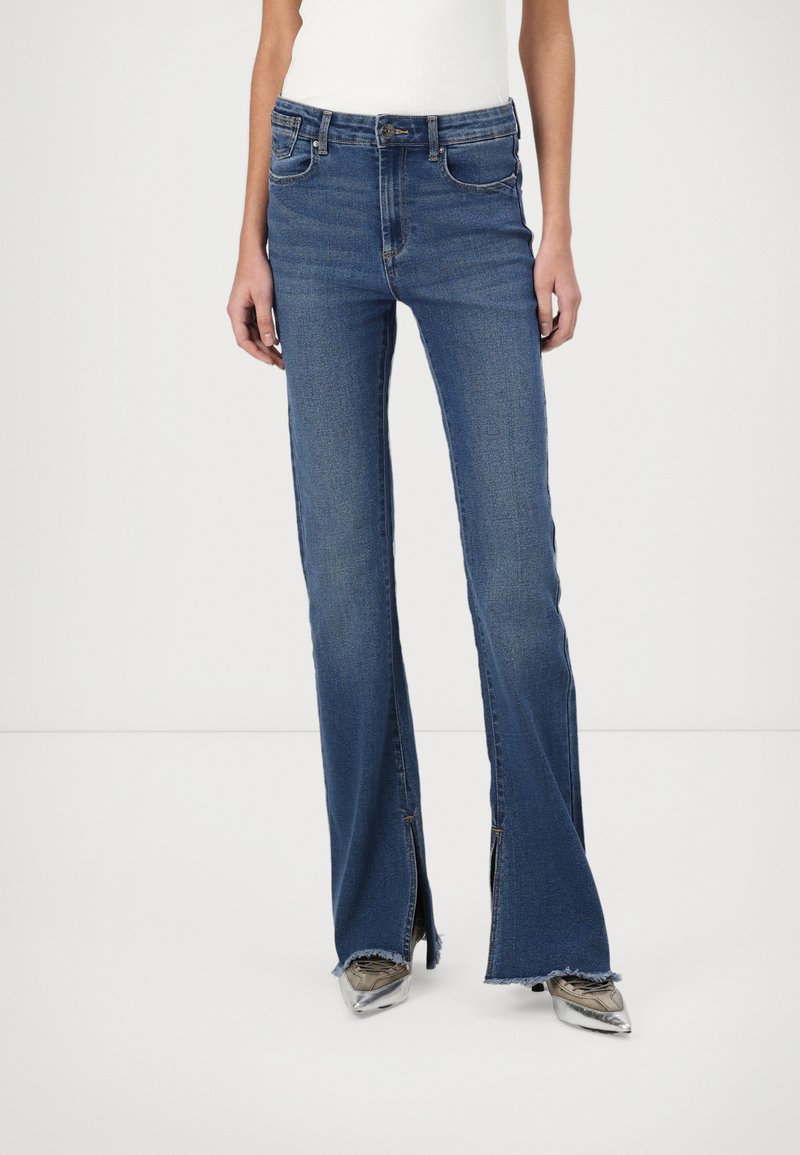 Jeans azuis de cintura alta em um tom desbotado, com pernas largas e fendas laterais na barra, apresentando o estilo clássico de cinco bolsos.