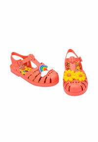 Sandalias de plástico coral brillante con diseño perforado, que presentan un arcoíris y una nube en un zapato y flores amarillas en el otro. Suela plana.