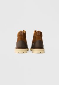 Braune Wildleder- und Lederstiefel mit einer beigen Gummisohle, die ein High-Top-Design und kontrastierende Nähte an der Ferse und an der Seite aufweisen.