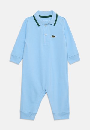 Barboteuse bébé bleu clair à manches longues, avec col polo bordé de vert et deux boutons, arborant un petit logo crocodile vert sur la poitrine.