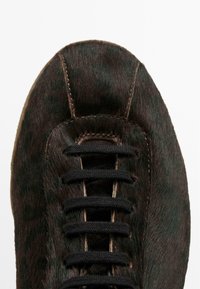 Sneaker marrone con una finitura morbida e pelosa, lacci neri e punta arrotondata. Accenti verdognoli notevoli sul materiale simile alla pelliccia.