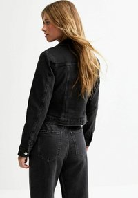 Chaqueta de mezclilla negra con diseño recortado, costuras visibles y dos bolsillos traseros. Textura suave y cierres de botón estándar en las mangas.