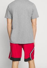 Camisa gris de manga corta combinada con pantalones cortos deportivos rojos que presentan detalles en negro y blanco y un logo negro en el dobladillo.