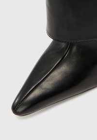 Čierna kožená členková čižma s hrotitou špičkou, hladkou textúrou a prešitým švom pri základe hornej časti čižmy.