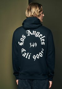 Sudadera con capucha de color navy con gran texto blanco en la parte posterior, que presenta "Los Angeles 349 Cali 900" en una fuente audaz y estilizada. Tejido suave.