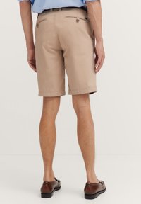 Beige Shorts von hinten gezeigt, aus glattem Stoff, mit zwei Gesäßtaschen mit Knöpfen und einem geraden Schnitt, der bis zur Mitte des Oberschenkels reicht.