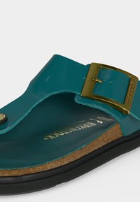 Σανδάλι Birkenstock σε χρώμα πετρόλ με χρυσή πόρπη, φελλό πάτο και μαύρη σόλα, με γωνία που δείχνει πλευρικές και επάνω λεπτομέρειες.