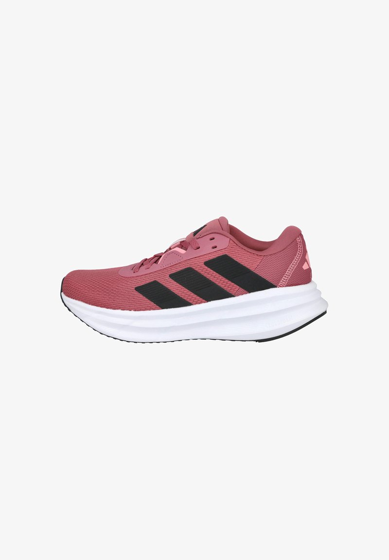 Zapatillas deportivas en rosa claro, con una parte superior de malla texturizada, tres rayas negras, una entresuela blanca acolchada y acentos en negro en la suela.