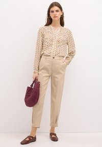 Camicia crema con bottoni e motivo floreale, pantaloni beige a vita alta, borsa bordeaux con texture e ballerine color porpora.