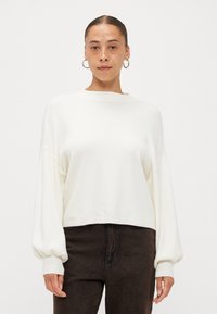 Weißer, kurzer Pullover mit langen, leicht puffigen Ärmeln und einem Boots-Ausschnitt, kombiniert mit dunkelbraunen Jeans. Weicher Stoff, minimalistisches Design.