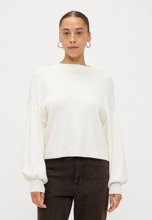Hvit cropped genser med lange, litt puffede ermer og båtutskjæring, kombinert med mørkebrune jeans. Myk tekstur, minimalistisk design.