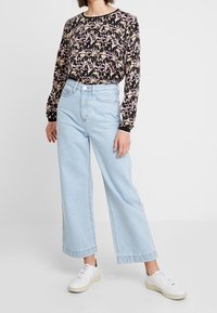 Blusa nera a maniche lunghe con stampa floreale, abbinata a jeans larghi azzurri e sneakers bianche. Outfit casual con vestibilità morbida.
