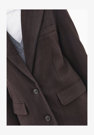 Blazer in tessuto a spina di pesce marrone con due bottoni frontali, due tasche laterali e colletto a revers. Indossato sopra un maglione grigio a collo a V.