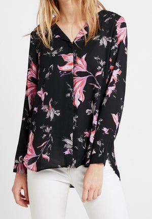 Sort bluse med lange ærmer, der har et blomstermønster i rosa og hvid. Knaplukning med en blød, glat tekstur.