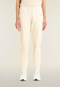 Pantalones de chándal color crema con textura acanalada, cintura elástica y detalle de cordón. Combinados con zapatillas deportivas blancas.