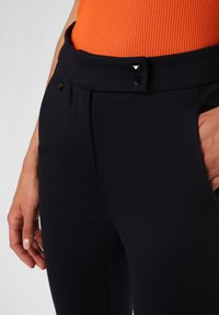 Navyblaue zugeschnittene Hosen mit glatter Textur, flachem Vorderteil, Seitentaschen und zwei schwarzen Pyramidennieten am Bund.