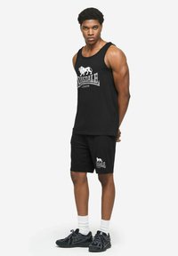 Czarny komplet z tank topem i szortami, z białym logo lwa i napisem. Gładka bawełniana tkanina, luźny krój. Dopełnieniem są sneakersy i białe skarpetki.