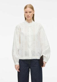 Witte katoenen blouse met lange pofmouwen, gerimpelde kraag, knopenvoorzijde en kantdetails. Gecombineerd met een donkere spijkerbroek en een clutch.
