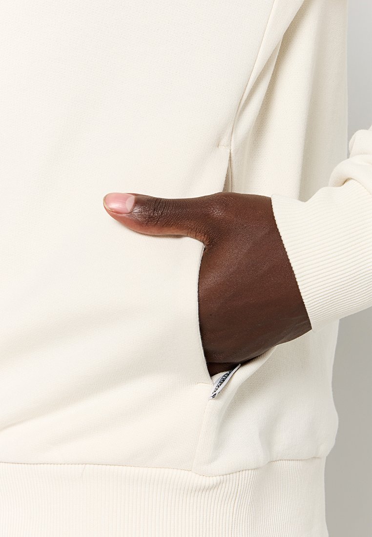 Felpa color crema con tasca laterale con chiusura a zip. Maniche a costine e un tessuto liscio e elastico.