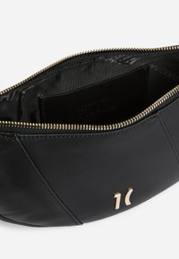 Borsetta in pelle nera con cerniera e logo metallico sul davanti, parzialmente aperta mostrando la fodera interna in tessuto nero e la tasca interna.