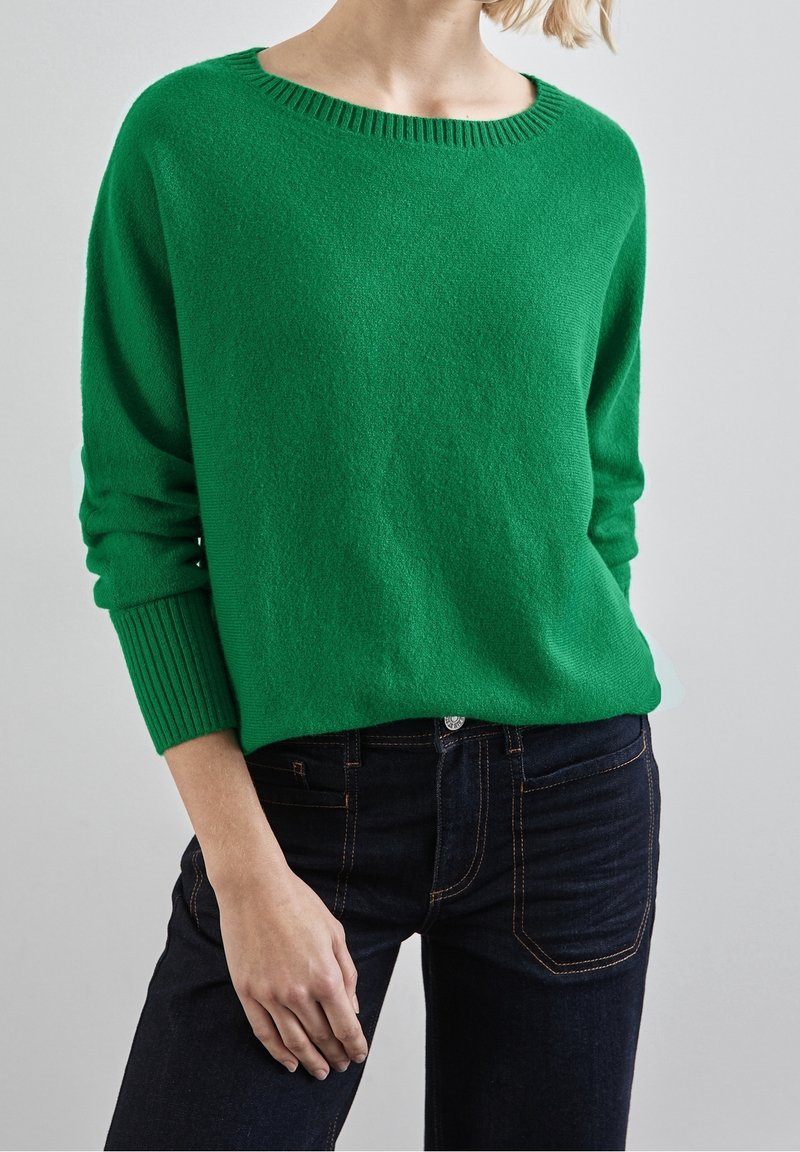 Grön stickad tröja med ribbad halsringning och muddar, som har en avslappnad passform. Tillsammans med mörk denimjeans. Mjuk struktur, avslappnad design.