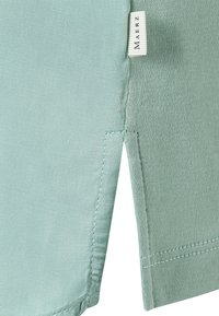 Mint green woven fabric with a smooth texture; features a side slit and a sewn label with the brand name at the hem.