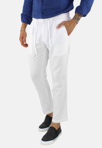 Pantaloni bianchi in lino con vita regolabile tramite cordoncino e tasche laterali, dal taglio dritto e texture leggera. Abbinati a scarpe nere slip-on.